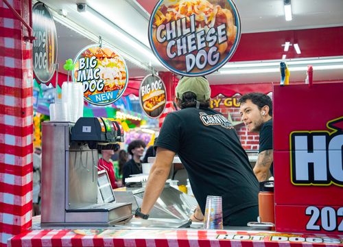 Free Lively scene at a food stall with staff serving chili cheese dogs at an outdoor event. Stock Photo