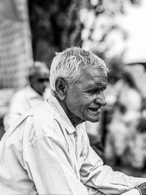 Free A candid black and white portrait of an elderly man with a gentle smile and white hair, captured outdoors. Stock Photo