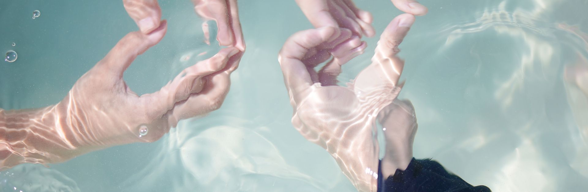 Three hands form shapes underwater with sunlight dancing on the skin.