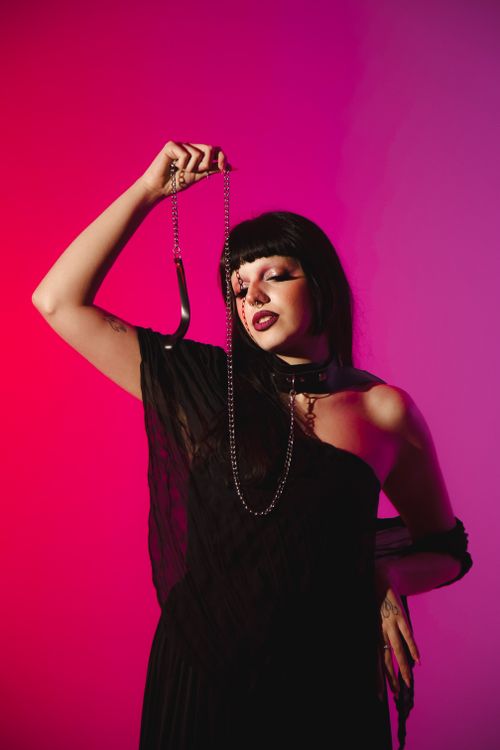 Free Portrait of a gothic-styled woman in dramatic pink and red lighting, holding a chain. Stock Photo