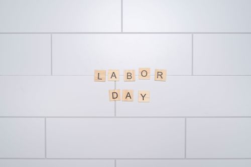 Free Wooden letter tiles spelling 'Labor Day' on a white tiled wall. Minimalist style. Stock Photo