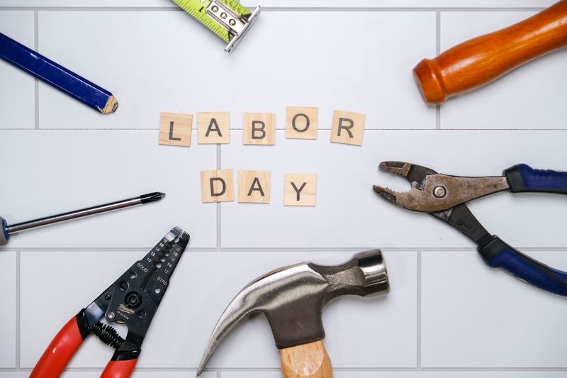 Creative flat lay of tools surrounding 'Labor Day' spelled out with Scrabble letters, symbolizing hard work.