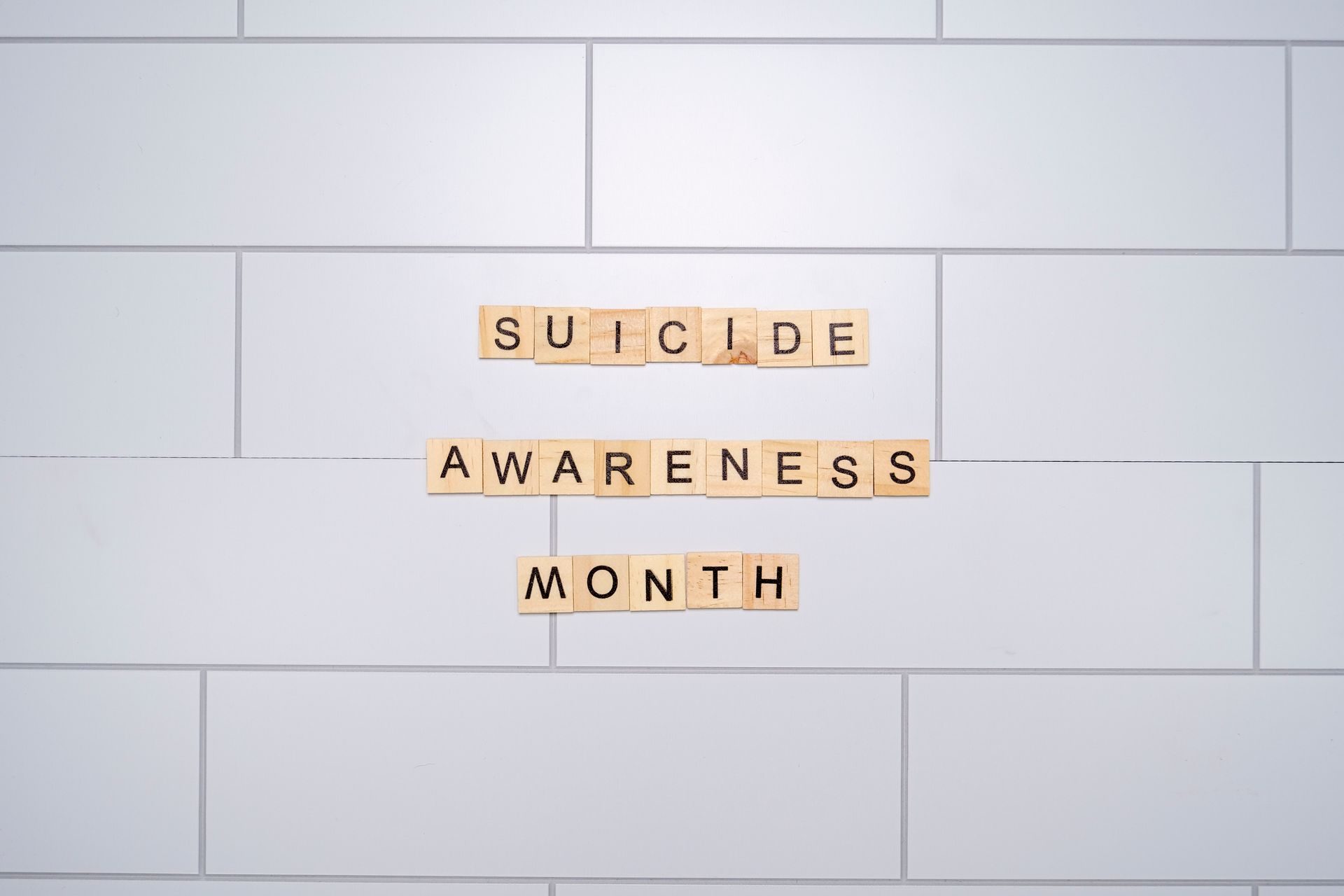 Suicide Awareness Month spelled with Scrabble tiles on a light background symbolizes mental health awareness.