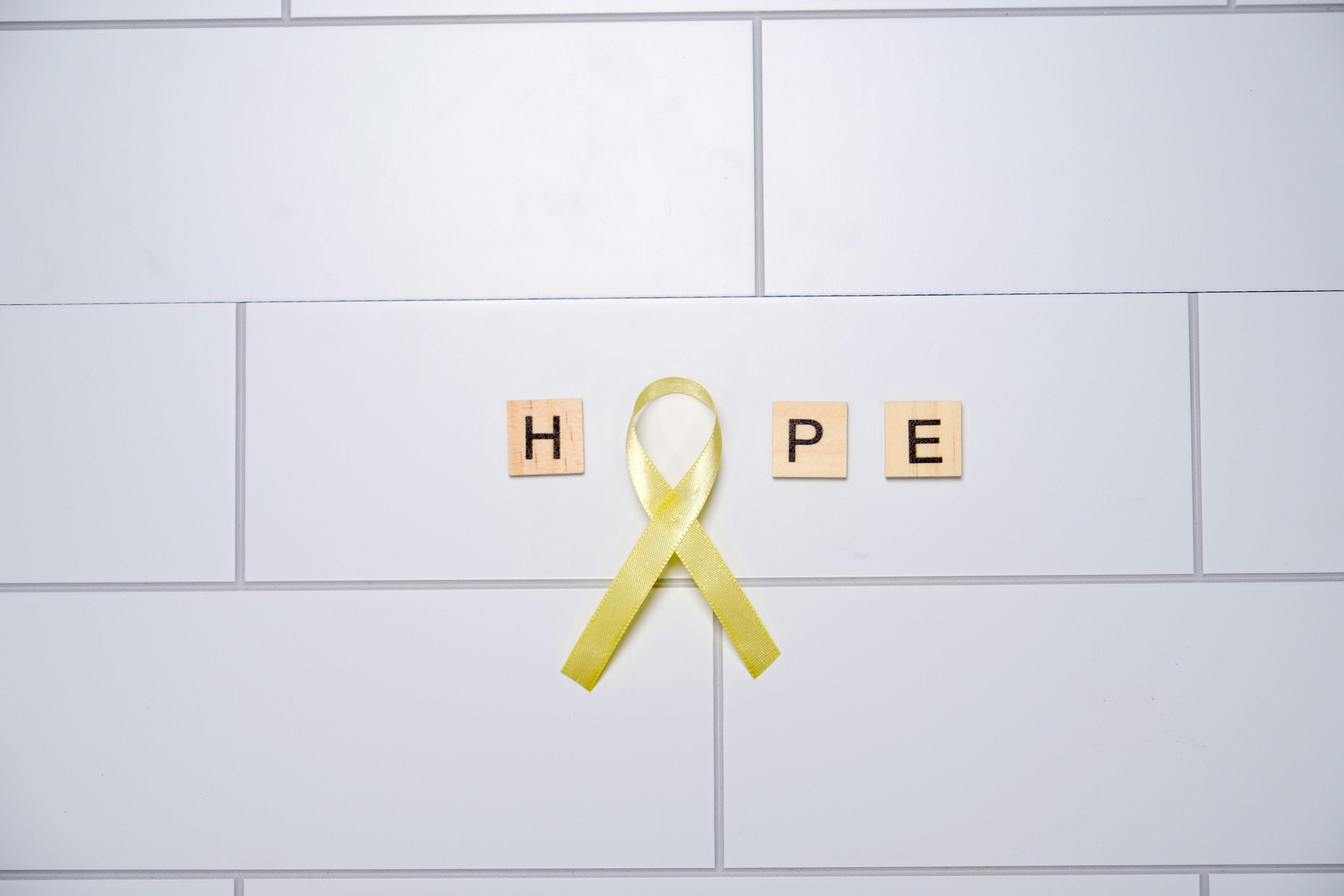 A yellow ribbon forming the word 'hope' with tiles on a white tiled background, symbolizing awareness and support.