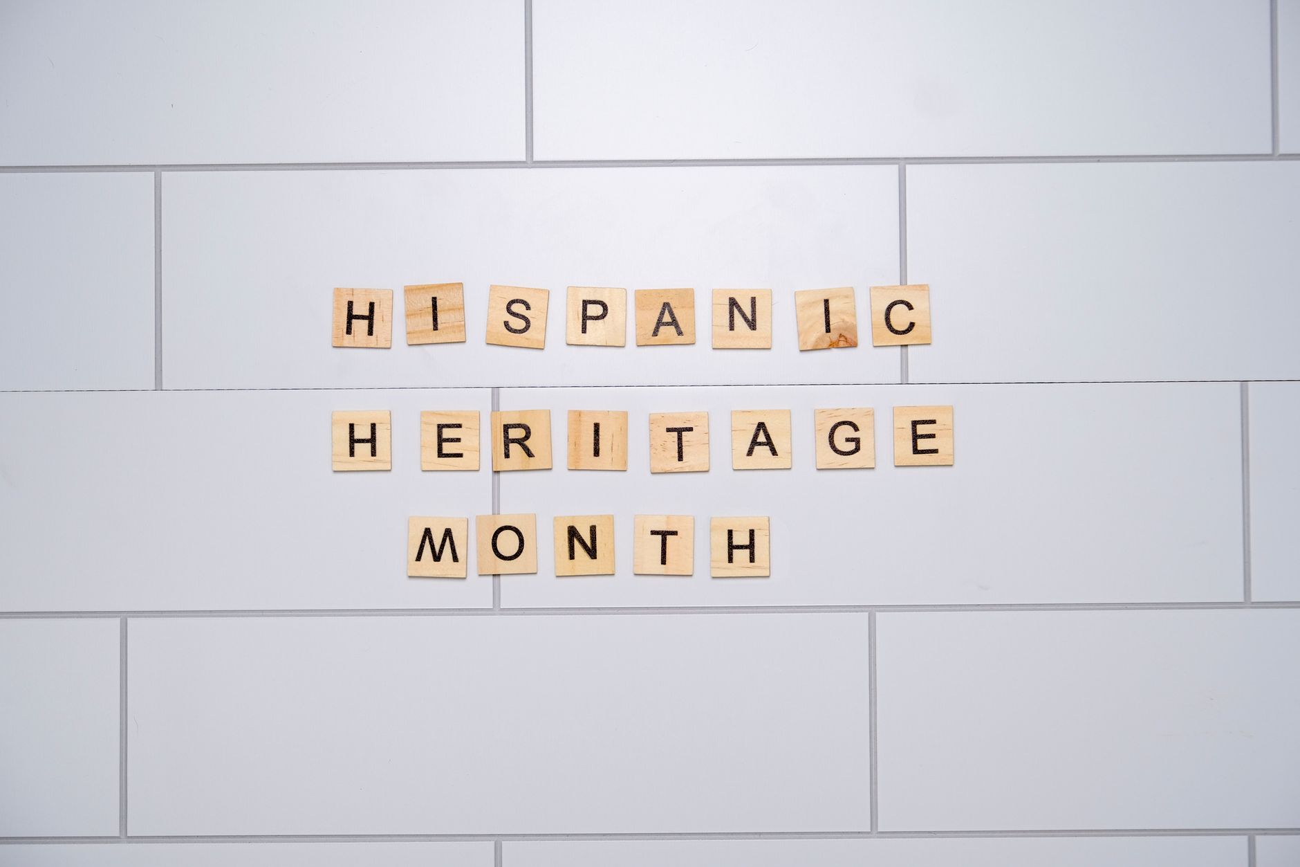 Wooden letter tiles spelling 'Hispanic Heritage Month' on a white tiled wall.