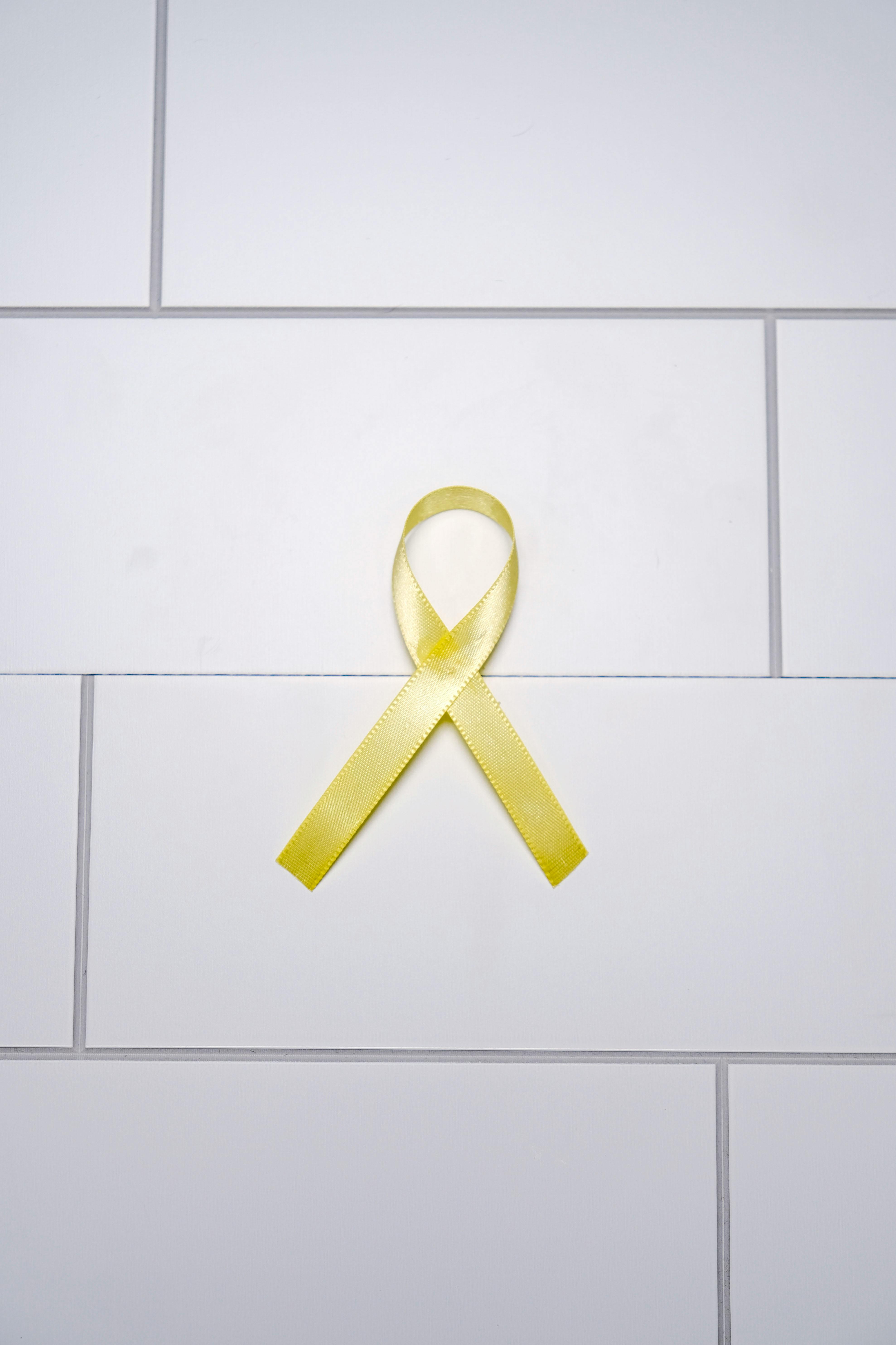 A yellow ribbon symbolizing awareness and support on a white tiled surface.