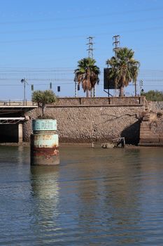 Riverside view in El Puerto de Santa María, showcasing palm trees and a stone wall.