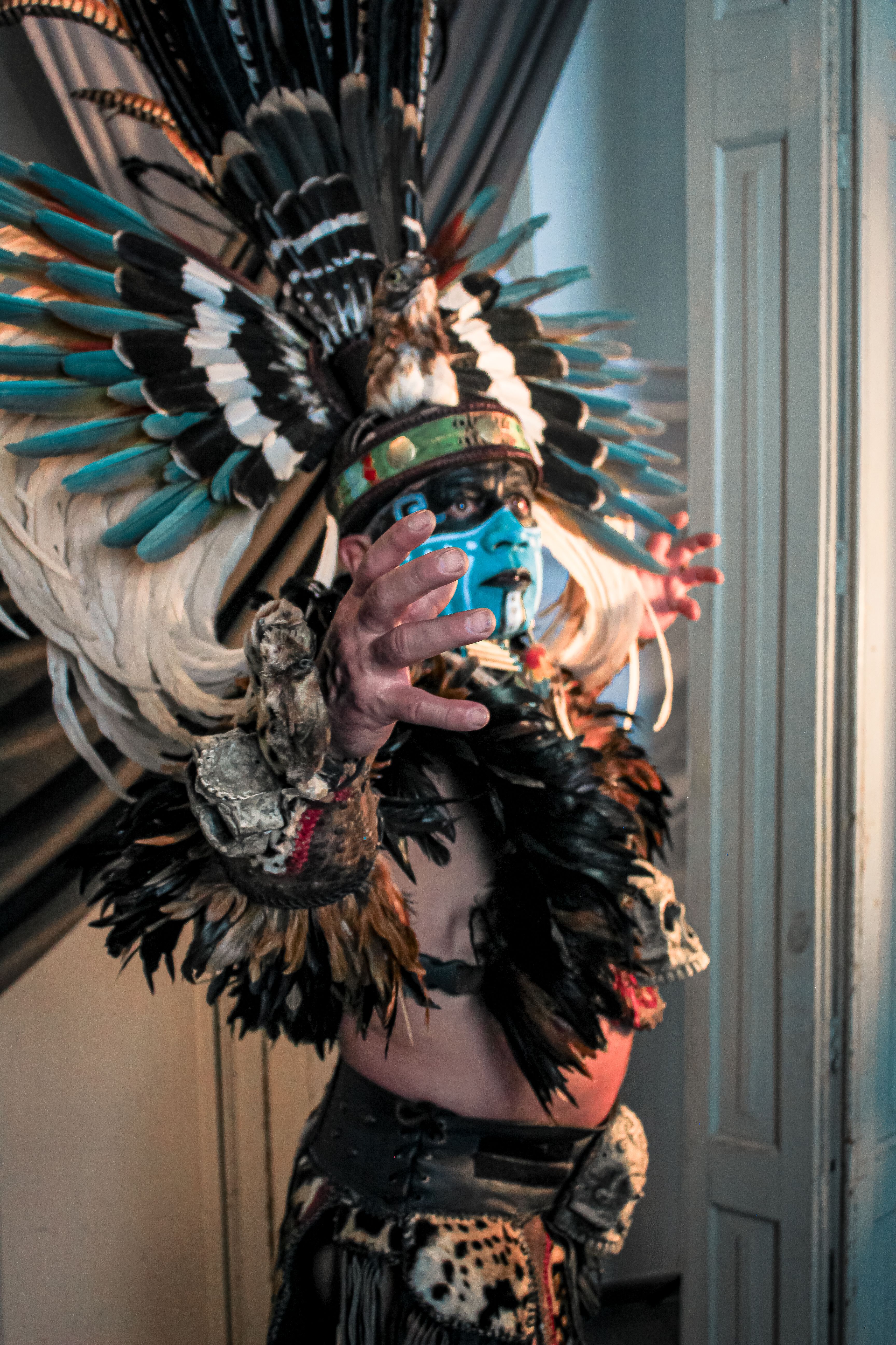 A colorful portrait of an indigenous person in traditional ceremonial attire inside a room.