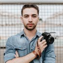 一个穿着牛仔布的年轻人拿着数码单反相机站在户外