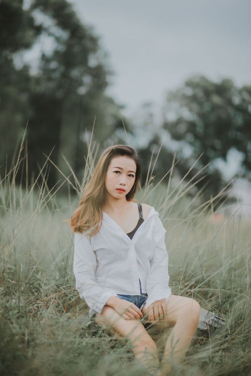 Free A fashionable woman poses gracefully in a grassy field, exuding elegance. Stock Photo