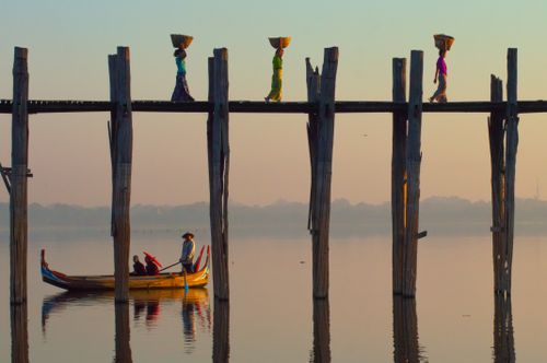 Free Women carrying baskets on U-Bein Bridge with a boat below at sunrise. Stock Photo