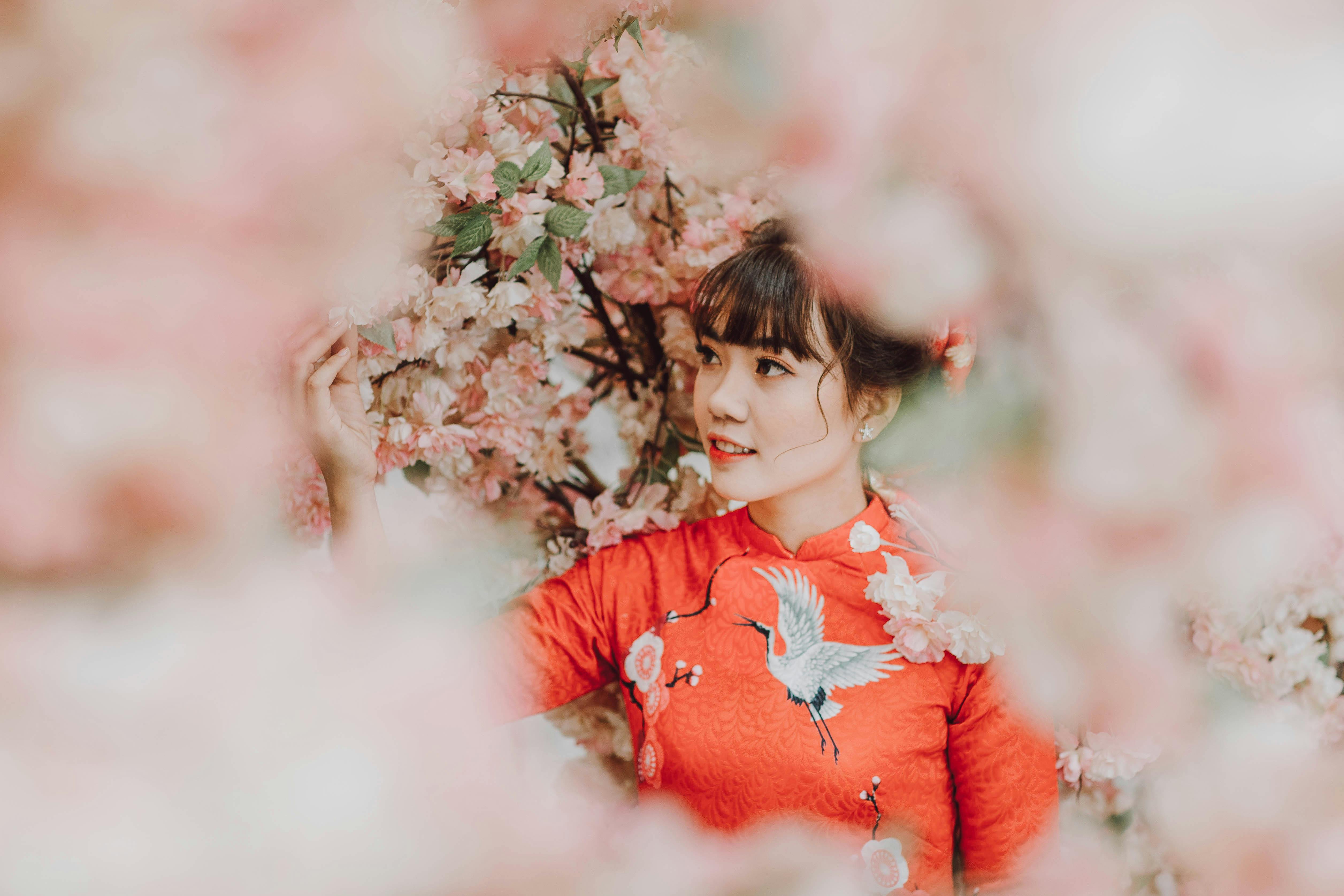 一名身穿鲜艳红色传统连衣裙的女子，在粉色樱花的环绕中，展露温暖的笑容