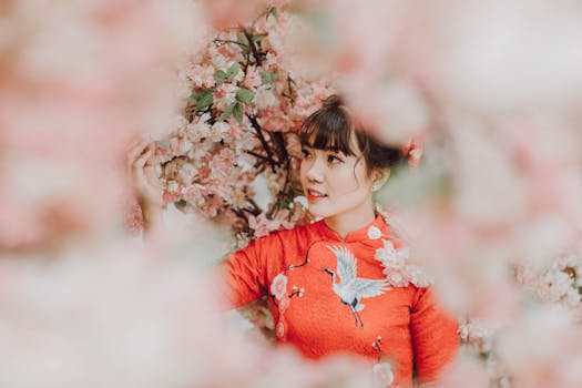 一名身穿鲜艳红色传统连衣裙的女子，在粉色樱花的环绕中，展露温暖的笑容