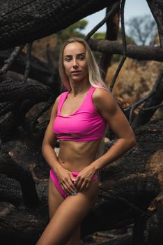 Portrait of a fit woman in a pink bikini standing amidst rugged nature.