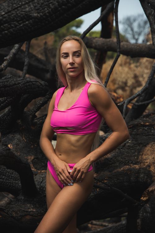 Free Portrait of a fit woman in a pink bikini standing amidst rugged nature. Stock Photo