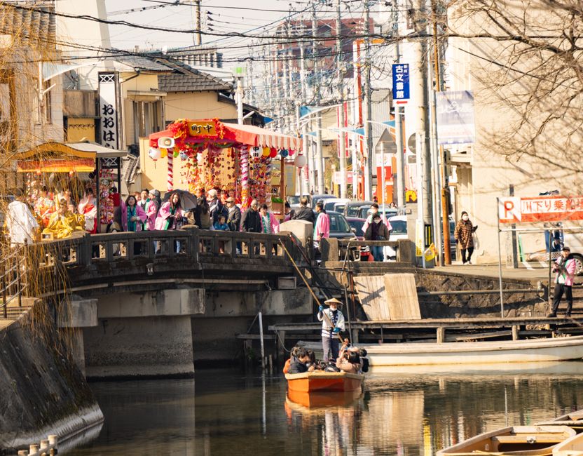 A lively canal scene in Fukuoka, Japan, showcasing a traditional festival with colorful decorations and people.