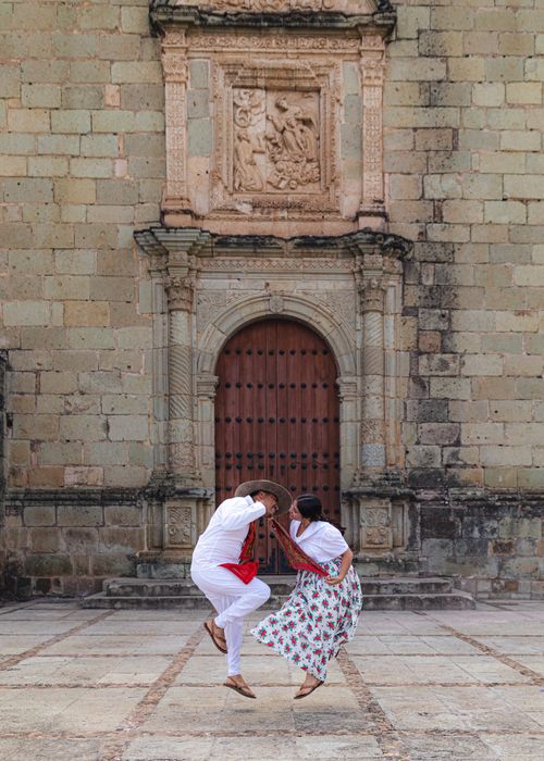 Free A couple performs a traditional dance in front of a historic stone building's ornate doorway. Stock Photo