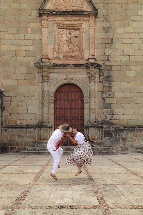 Free Joyful couple dancing in front of a historic stone building with an ornate archway. Stock Photo