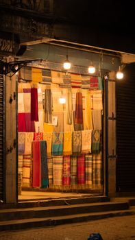 Colorful scarves and fabrics illuminated in a Kathmandu shop window at night.