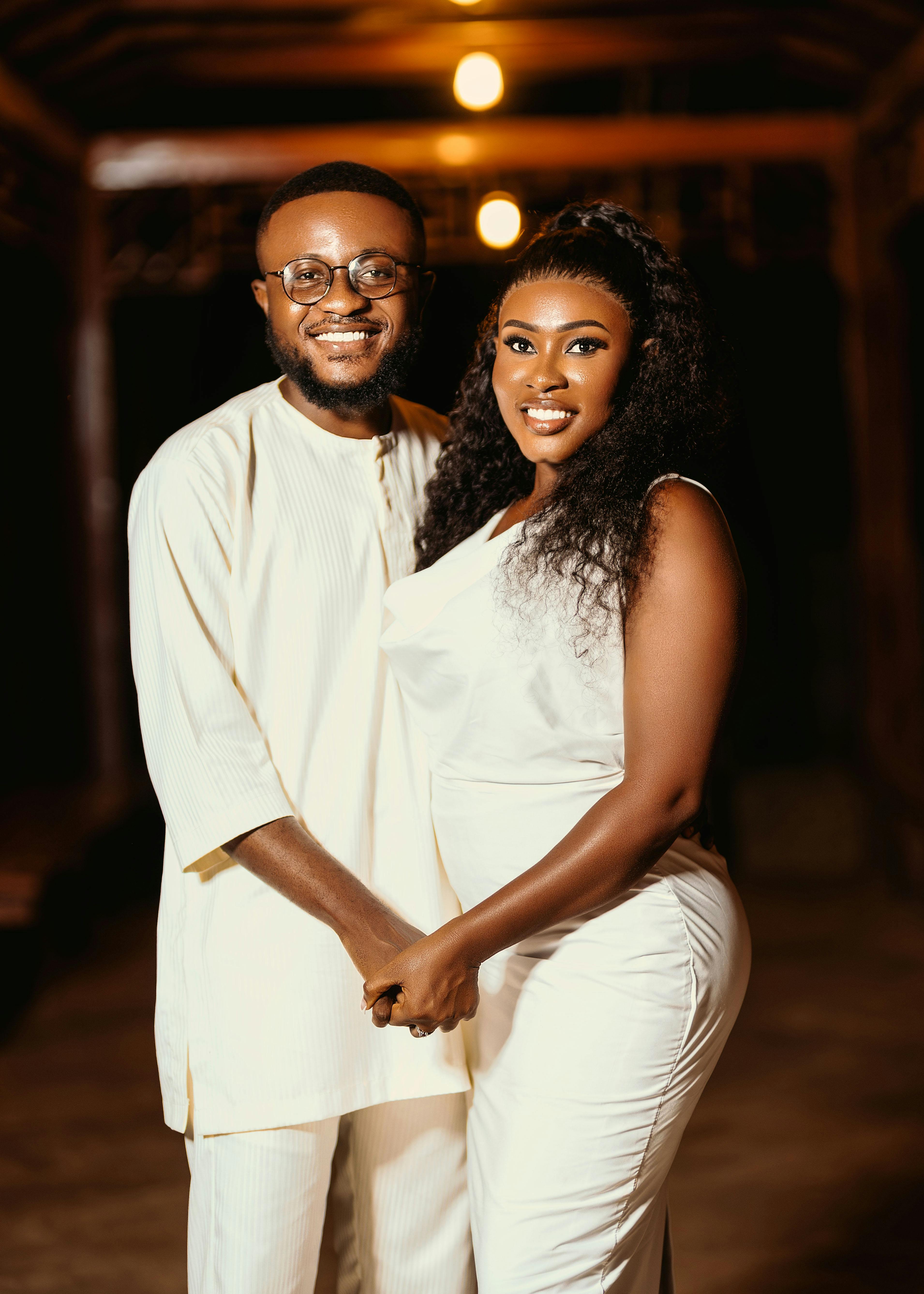 Charming young couple holding hands in elegant white attire, night setting.