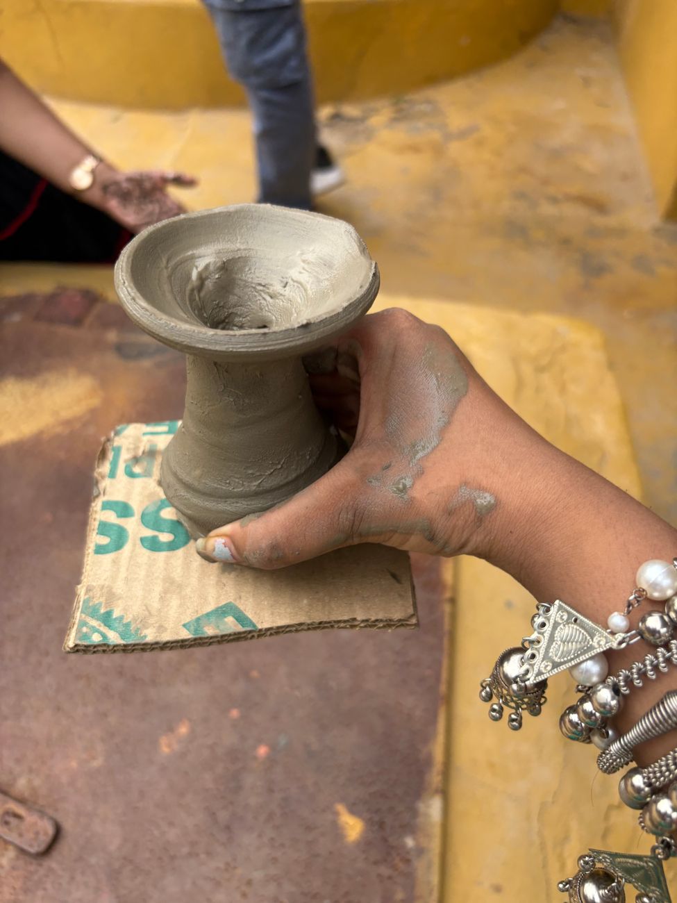 A person crafting a clay pot by hand, showing traditional pottery skills outdoors.