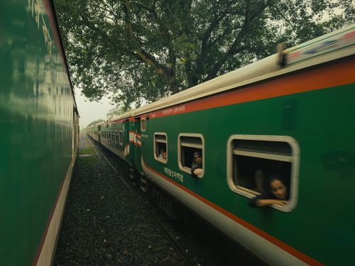 Free View of a speeding train with passengers looking out, surrounded by lush trees, captured from another moving train. Stock Photo