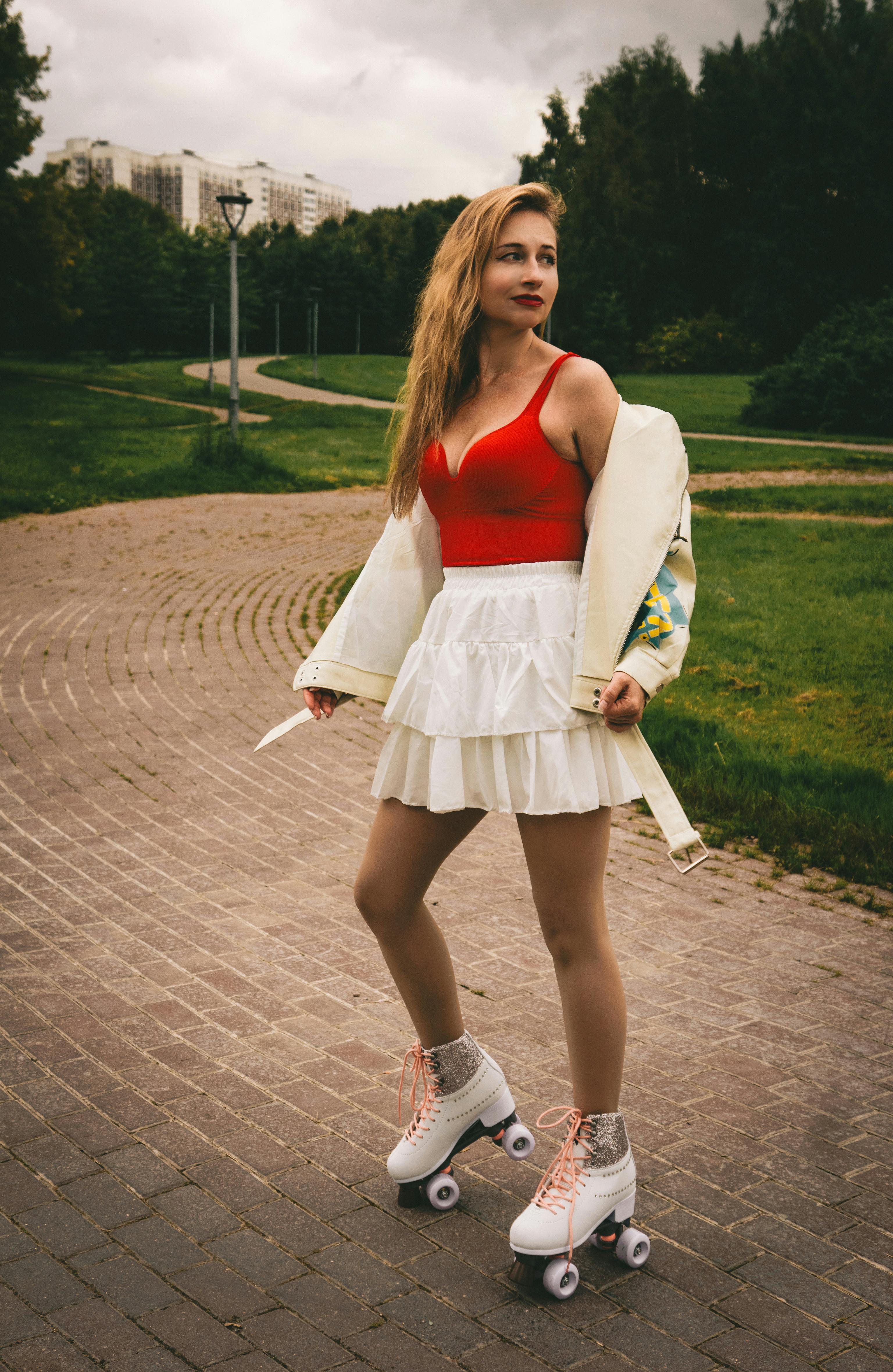 Young woman in red top and white skirt roller skating in a park, embracing outdoor fun.