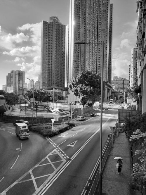 Free Black and white urban scene featuring skyscrapers, road, and pedestrian with umbrella. Stock Photo