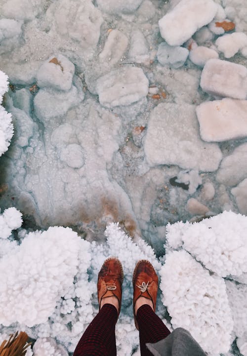 From above of crop anonymous female traveler in boots standing on rough surface covered by crystalline sea salt