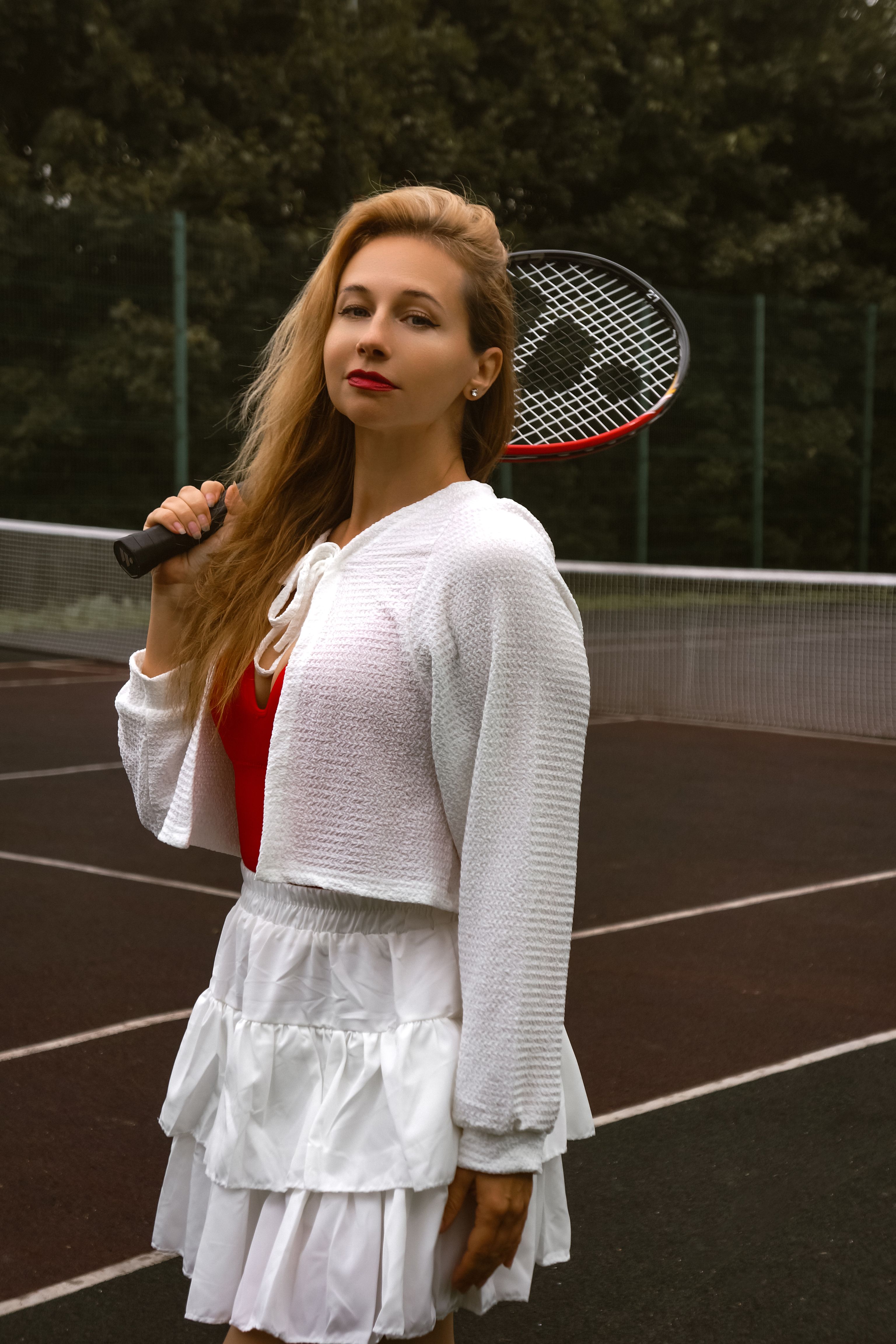 Woman in tennis attire posing confidently with racket on outdoor court.