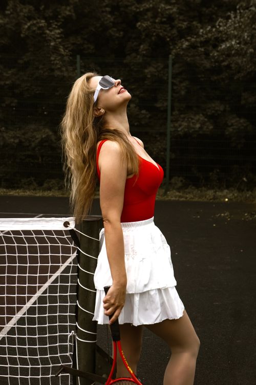 Free Elegant female tennis player in sporty attire leaning on net, enjoying a sunny day outdoors. Stock Photo