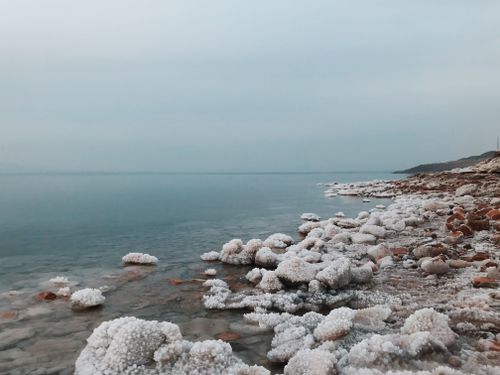 Free Peaceful scenery of calm Dead Sea with natural mineral salt formations and stones against cloudy sky Stock Photo