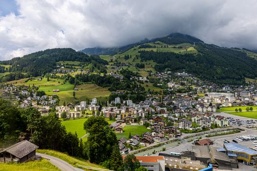 Aerial view of Engelberg, Switzerland, with lush green hills and cloudy skies.