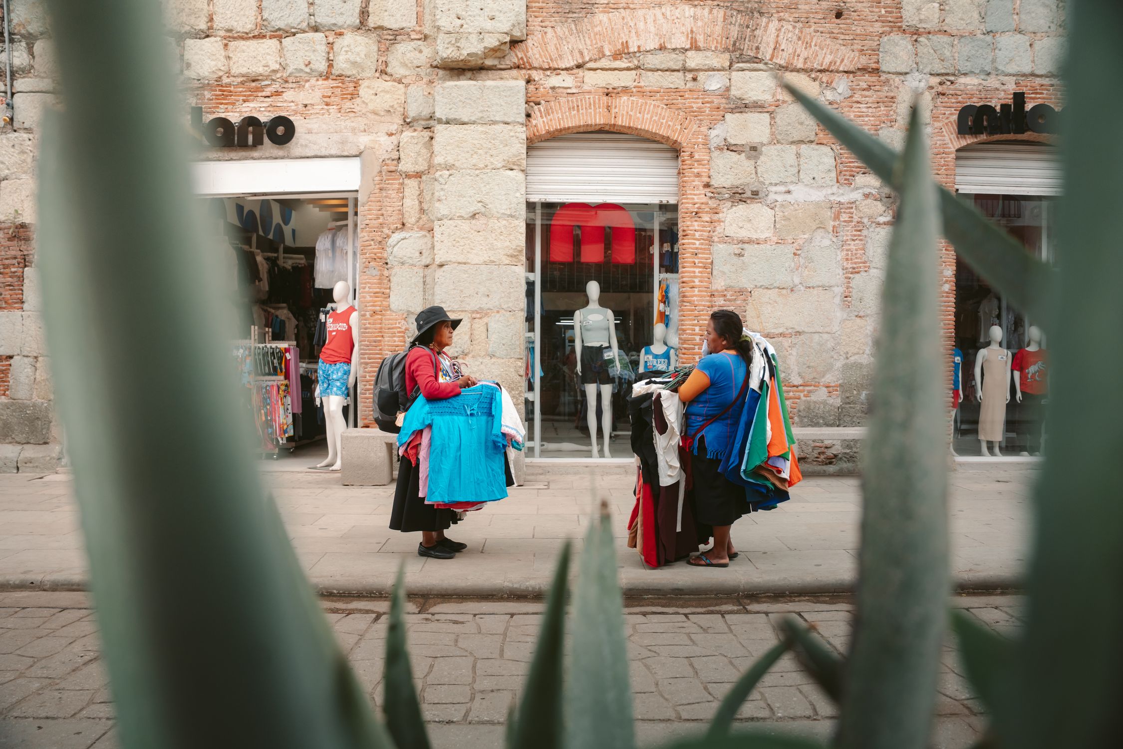 Colorful street scene in Oaxaca featuring local vendors selling clothing near a boutique.