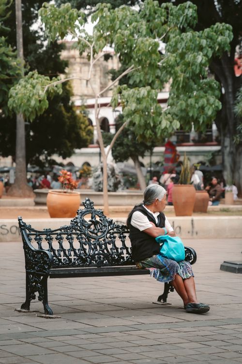 Free An elderly woman sits alone on a decorative bench in Oaxaca city park. Stock Photo