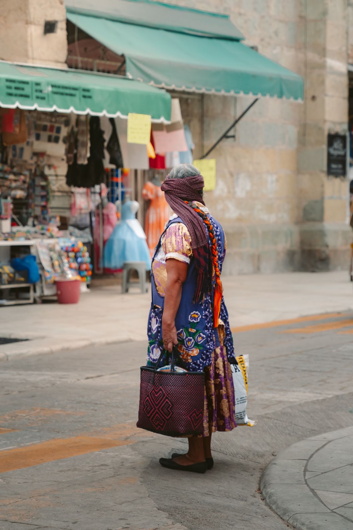 A woman in traditional attire stands by a vibrant market in Oaxaca, Mexico.