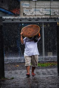 A person walks through the rain in West Java, Indonesia, using a woven basket for cover.