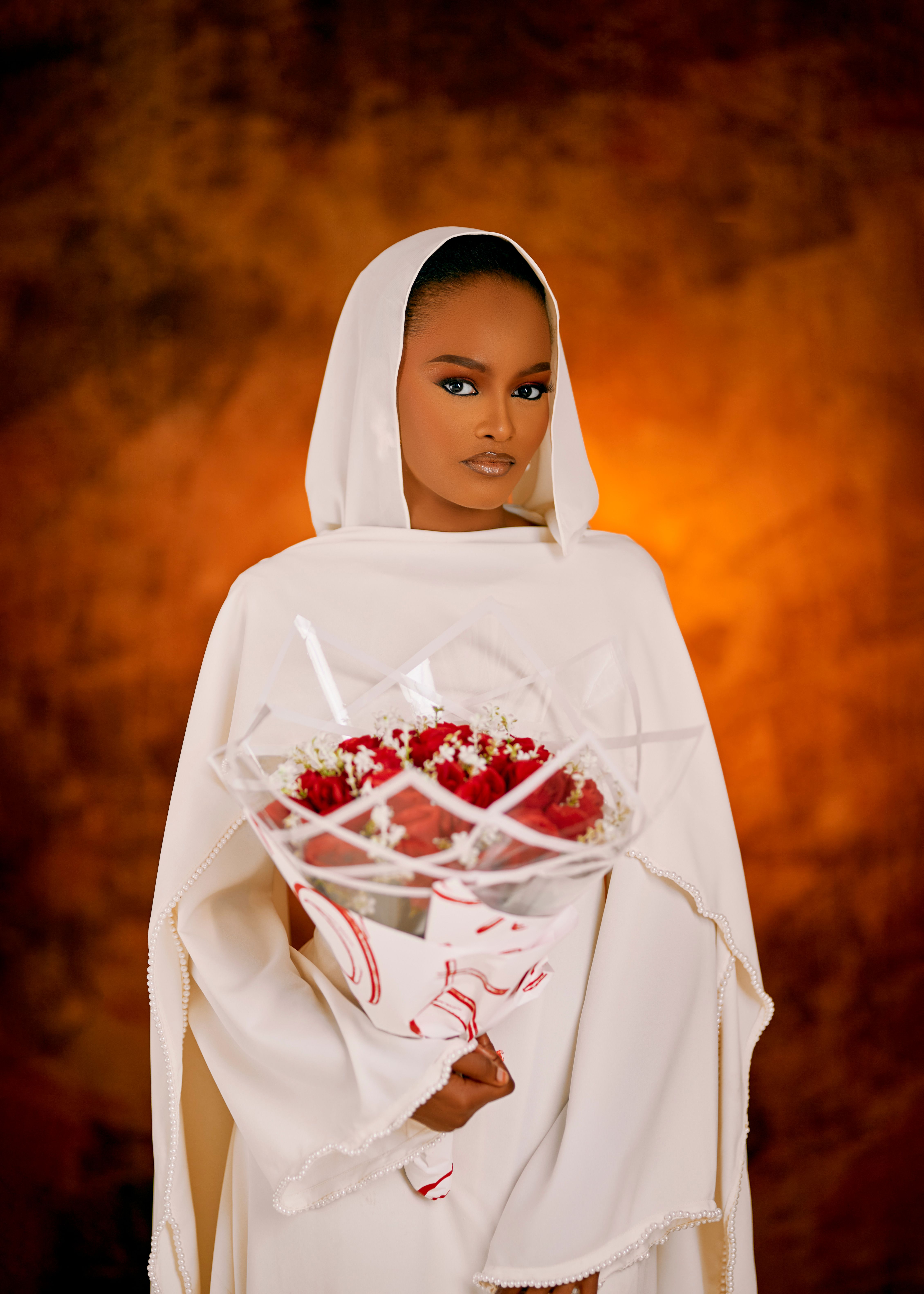 A woman in a white traditional dress holding a bouquet against a warm background.