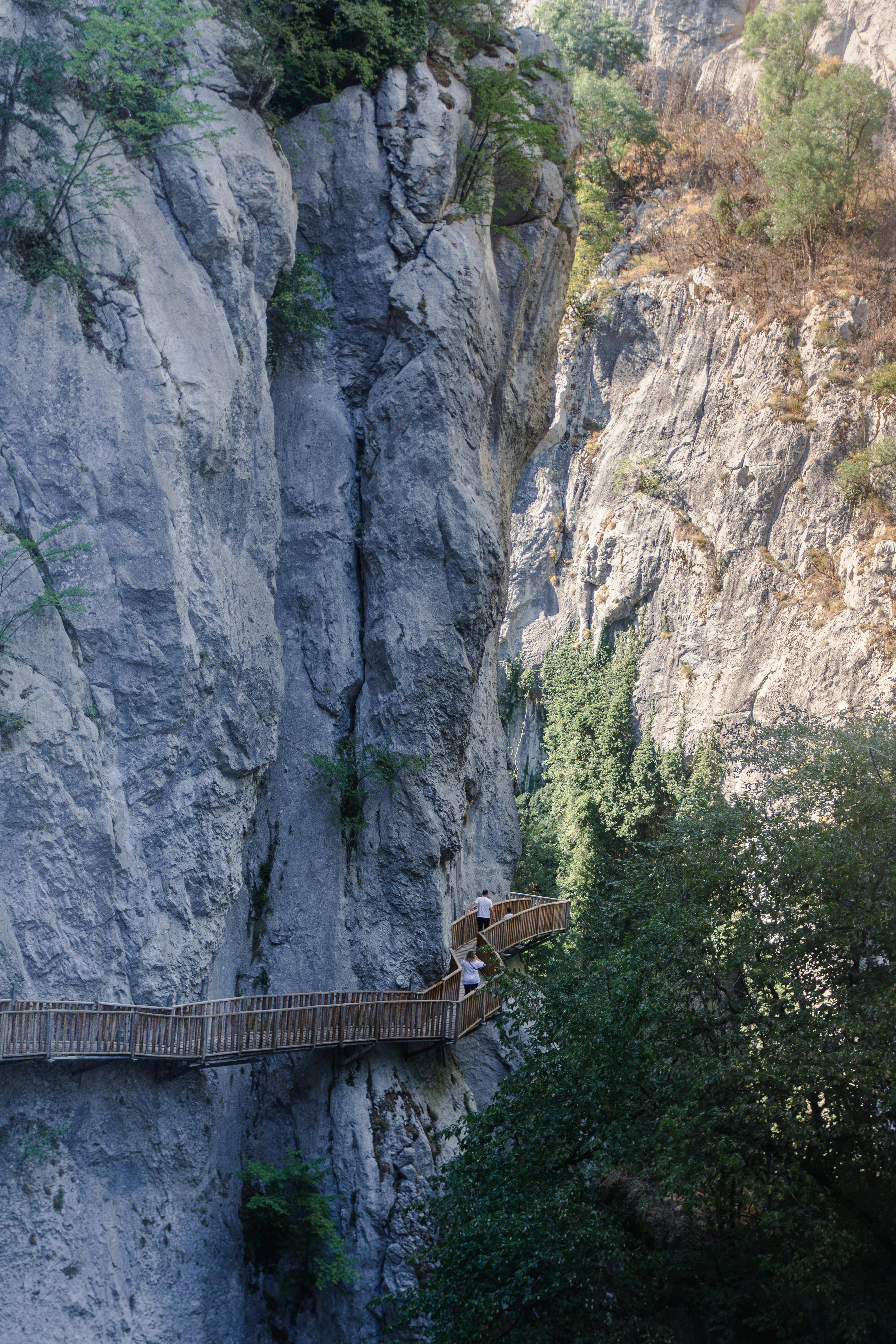 Hikers on a wooden pathway carved into a dramatic canyon cliff, showcasing breathtaking natural scenery.