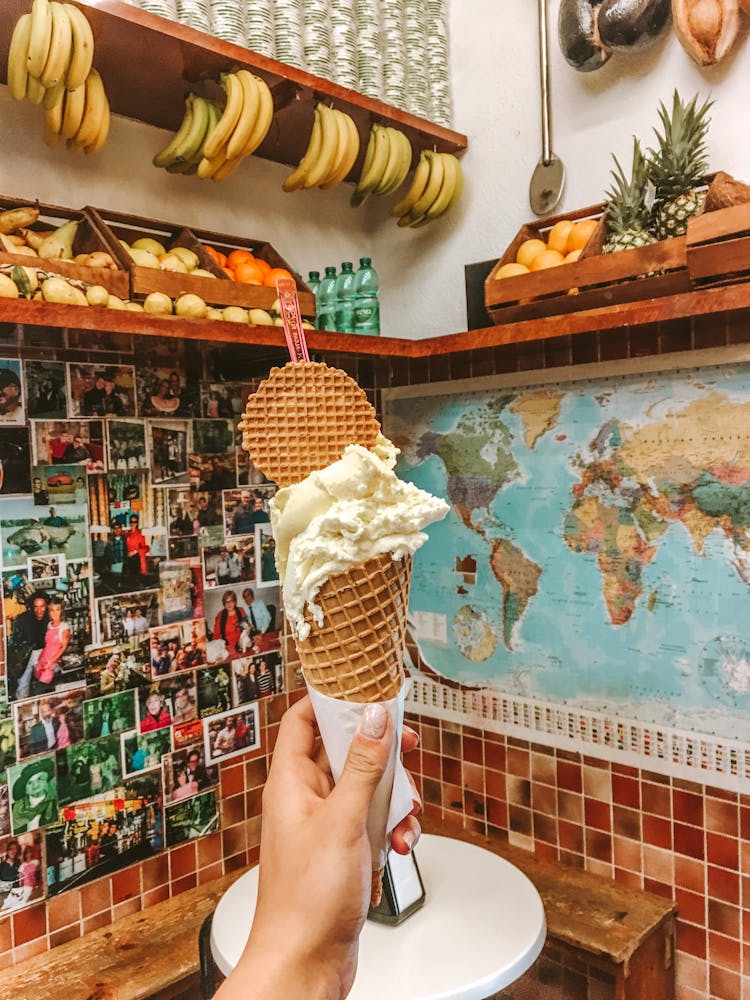 Hand Holding Ice Cream Cone Inside Colorful Market