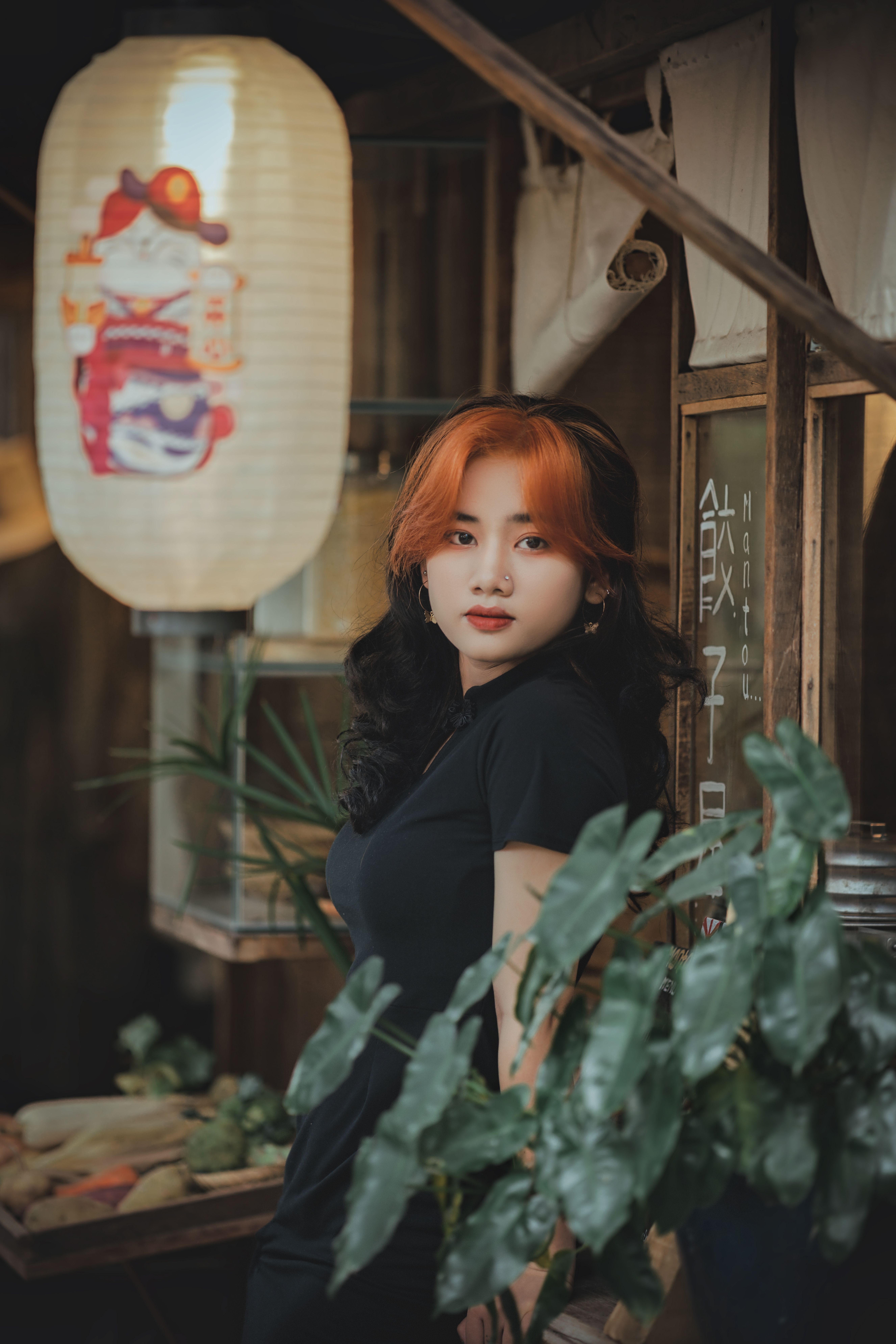 Portrait of a woman with auburn hair in a traditional Asian interior setting, surrounded by plants and decor.
