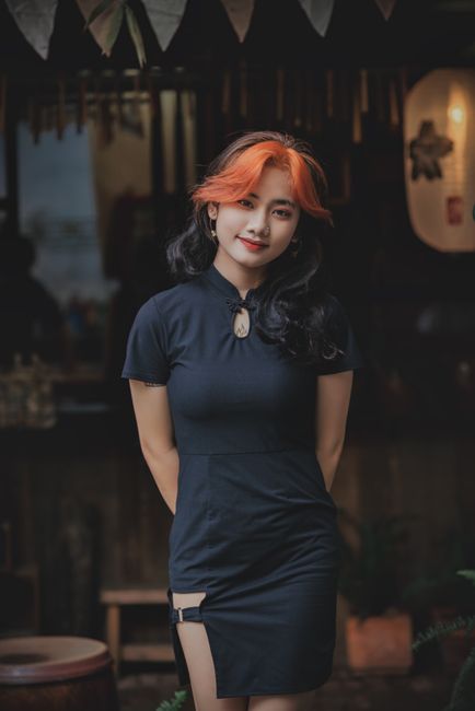 Elegant young woman poses outdoors in chic black dress with vibrant hair.