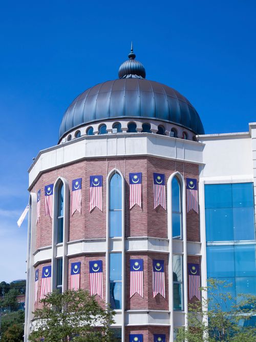 Free Modern building adorned with Malaysian flags under a bright blue sky, showcasing architectural elegance. Stock Photo