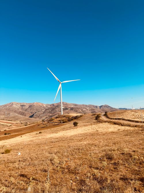 Free Clean energy wind turbine on a sunny, hilly landscape with clear blue skies. Stock Photo
