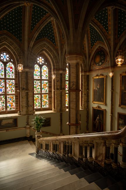 Neo-Gothic staircase with ornate stained glass windows in a historic Scottish building.