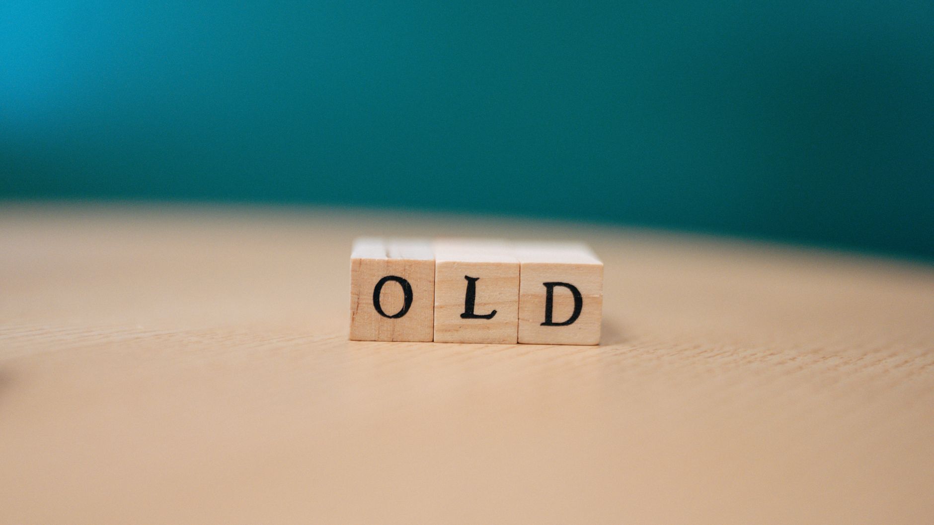 Wooden blocks on a table spelling "OLD" with a plain background.
