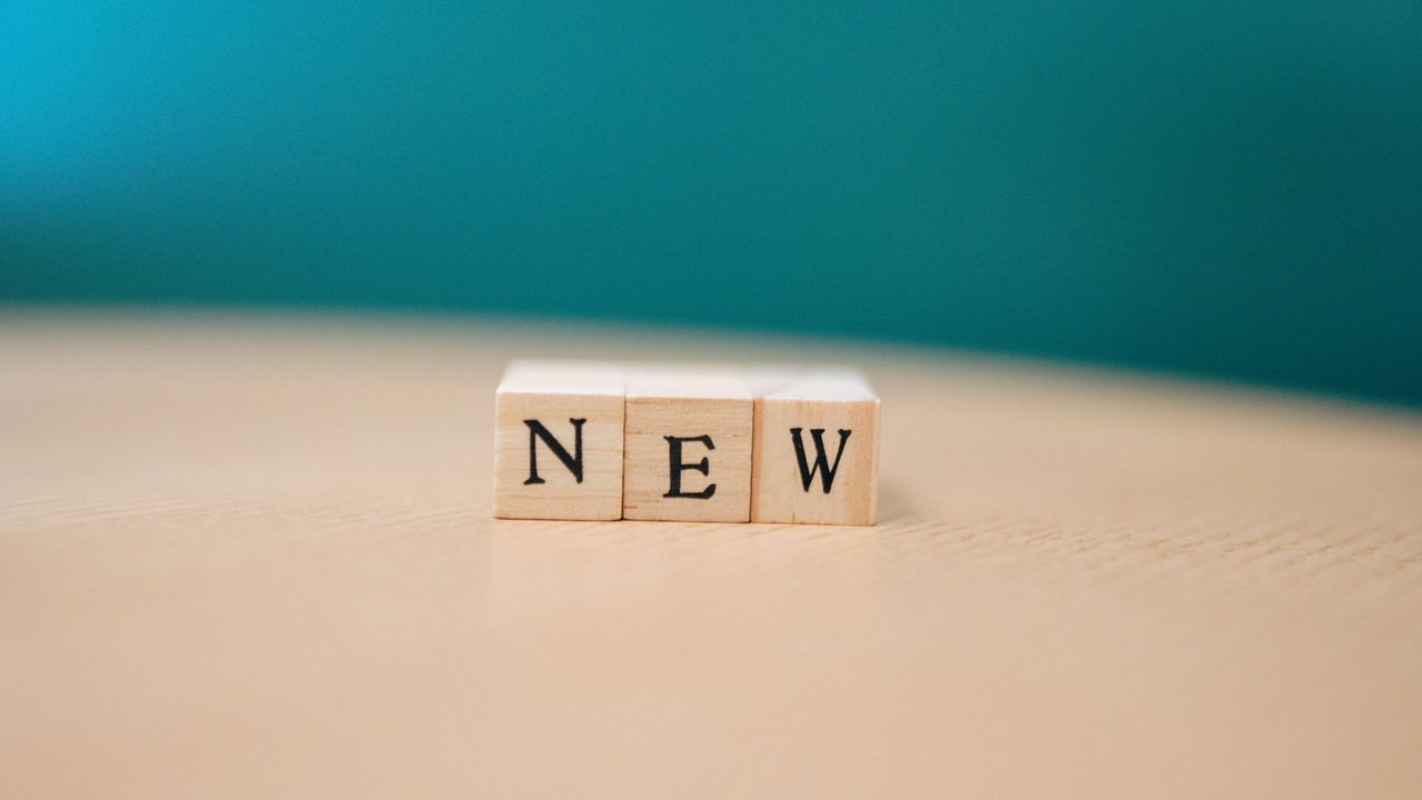 wooden blocks spelling out new on a wooden surface against a teal back