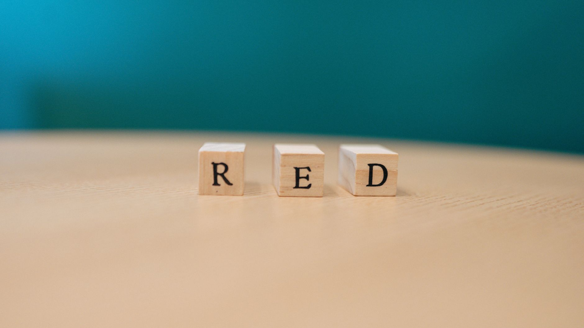 Close-up of wooden blocks spelling 'RED' on a table with teal background.