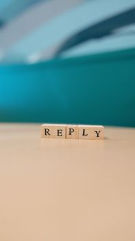 Wooden blocks spelling 'reply' on a table with blurred background.