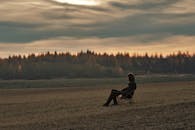 日落时分，一个人孤独地坐在宁静的乡村田野的椅子上，心中一片平静